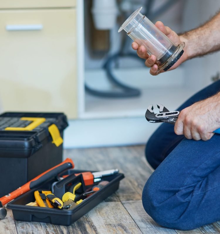 Plumbing done right. Cropped shot of professional plumber using pipe wrench and other tools while fixing sink pipe in the kitchen. Repair service and plumbing concept. Side view. Horizontal shot