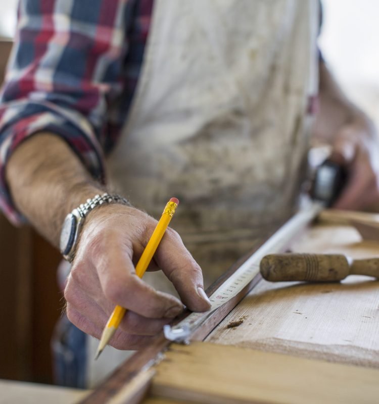 An antique furniture restorer measuring a piece of wood.