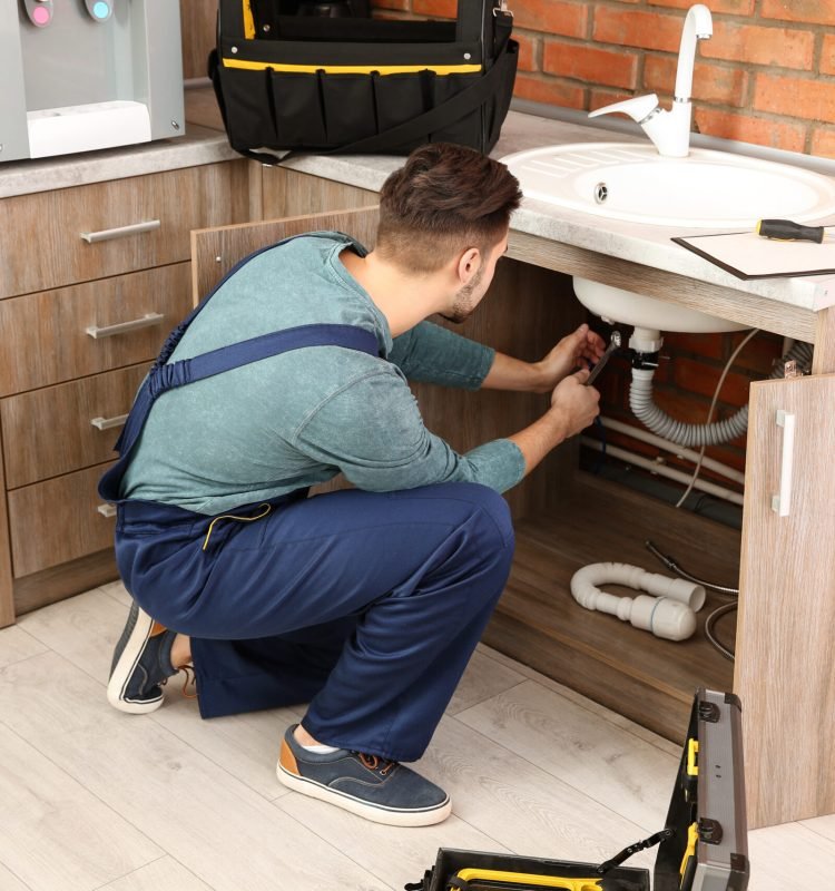Male plumber in uniform repairing kitchen sink