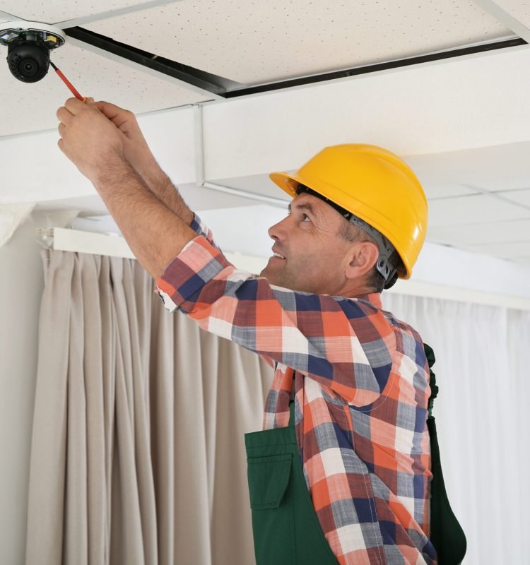 Electrician with screwdriver repairing CCTV camera indoors