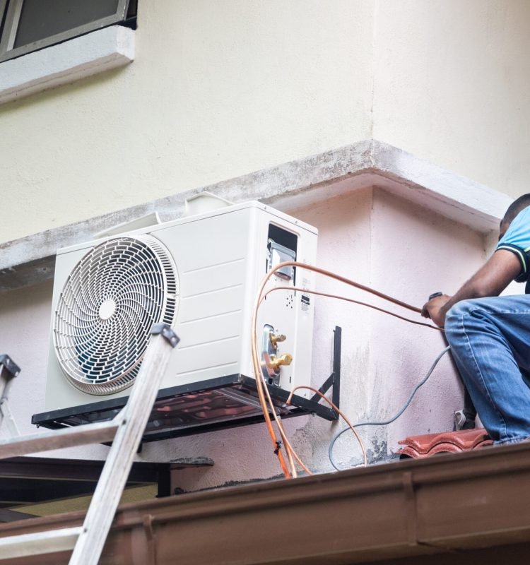 Technician installing outdoor air conditioner compressor unit on outdoor wall