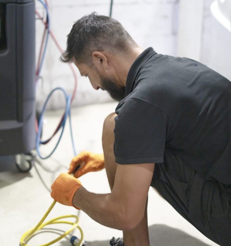Male auto mechanic in protective gloves handles cables while repairing a vehicle
