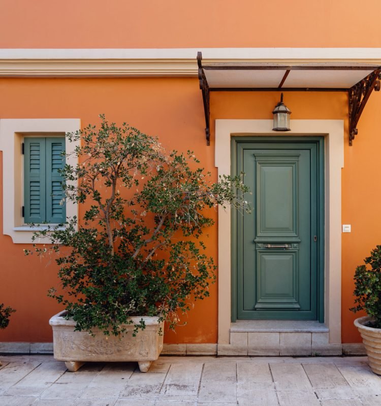 The warm facade of a Mediterranean home with green shutters and potted plants creates an inviting entrance