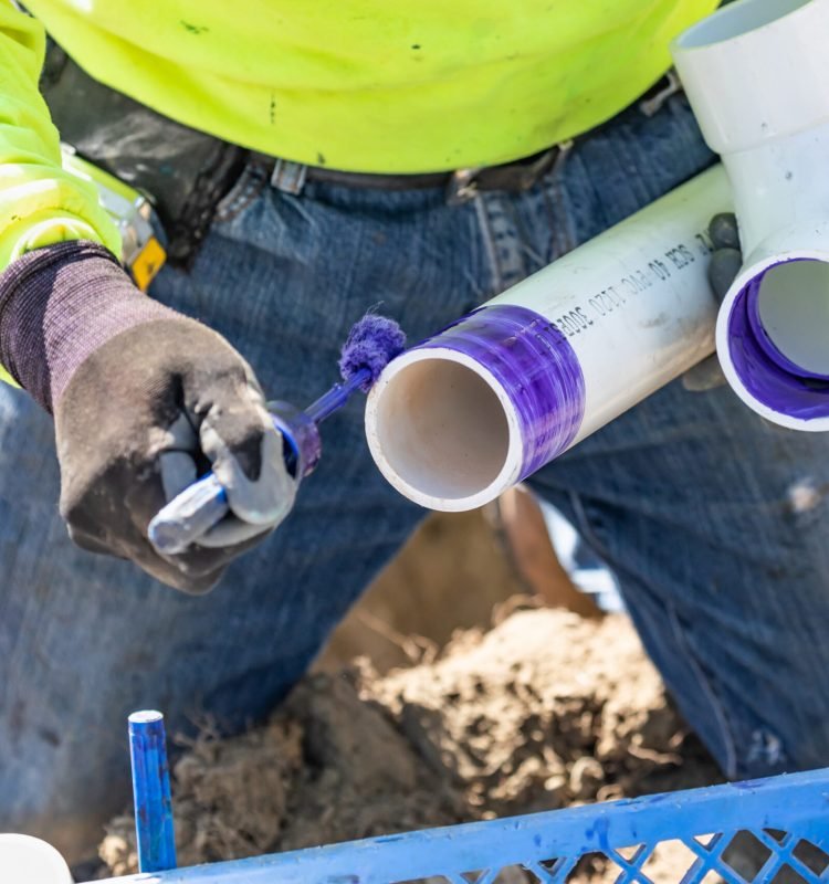 Plumber Applying Pipe Cleaner, Primer and Glue to PVC Pipe At Construction Site.